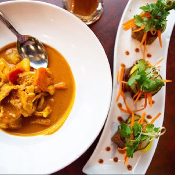 A bowl of Narunya's Thai yellow curry with chicken and vegetables, alongside three appetizers.