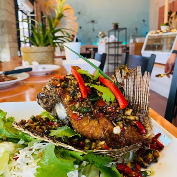 Whole fried fish with chili garlic sauce and fresh herbs on a white plate at Narunya's.