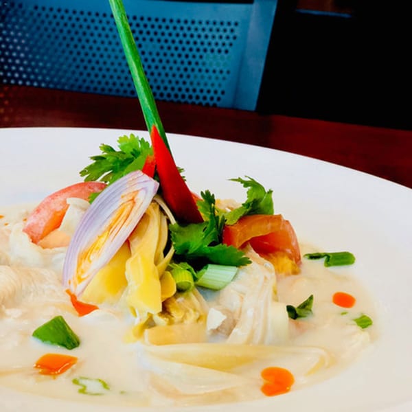 Narunya's Thai coconut soup with chicken, red chili, shallots, and herbs in a white bowl.