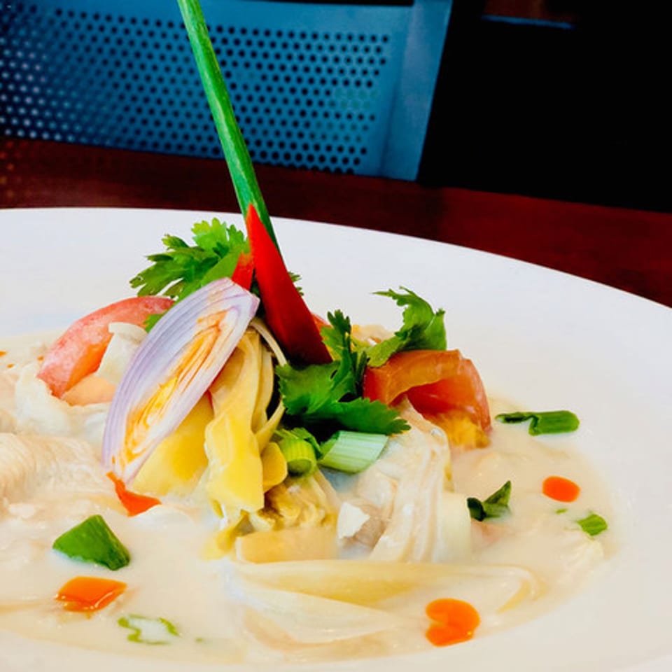 Narunya's Thai coconut soup with chicken, red chili, shallots, and herbs in a white bowl.